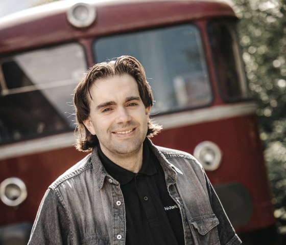 "Bahnhofsvorsteher" Andreas Kurth vor seiner historischen roten Bahn
, © Andreas Kurth Ein Mann steht vor einer historischen roten Bahn und schaut in die Kamera.