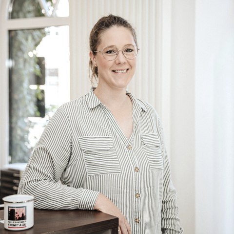 Malin Blomenkamp, Mitarbeiterin der Touristik GmbH Gerolsteiner Land, stellt sich vor.
, © Laura Kirwel  Eine Frau steht hinter einem Tresen und lächelt in die Kamera. Hinter ihr einige Fenster und Regale mit regionalen Produkten.