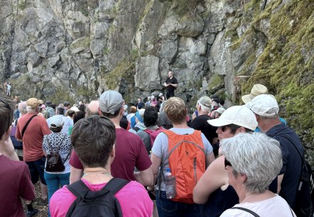Jens Koppka berichtet über die geologischen Gegebenheiten vor Ort, © Touristik GmbH Gerolsteiner Land Zahlreiche Wanderer vor einer massiven Steinwand. Der Tourguide erzählt über die geologischen Gegebenheiten vor Ort.