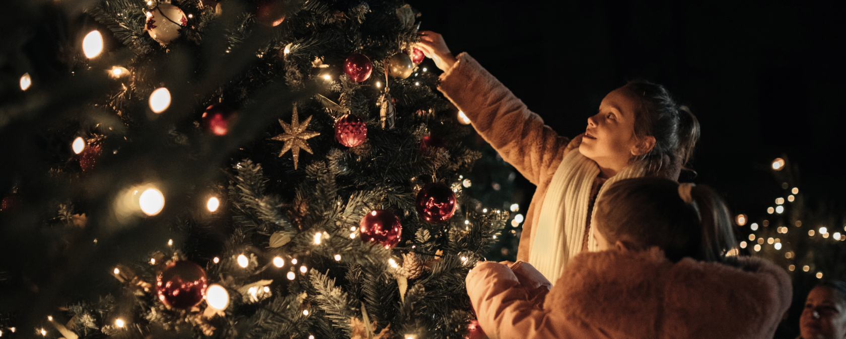 zwei Kinder schmücken einen Weihnachtsbaum mit Kugeln. Der baum leuchtet schon in der Dunkelheit, © Touristik GmbH Gerolsteiner Land zwei Kinder schmücken einen Weihnachtsbaum mit Kugeln. Der baum leuchtet schon in der Dunkelheit, © Touristik GmbH Gerolsteiner Land