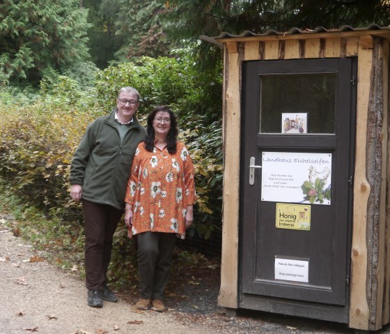 Herr und Frau Pick neben dem Verkaufshäuschen des Landhaus Eichelseifen.
, © Touristik GmbH Gerolsteiner Land Ein Mann und eine Frau stehen neben einem kleinen Holzhaus mit Aufschrift Landhaus Eichelseifen.
