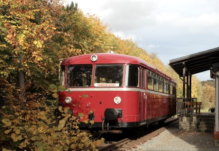 Historic red train in front of the Ahütte museum station.
, © Andreas Kurth A historic red train with a sign saying ‘Special trip’ is parked on the tracks next to an old station building in autumn weather.
