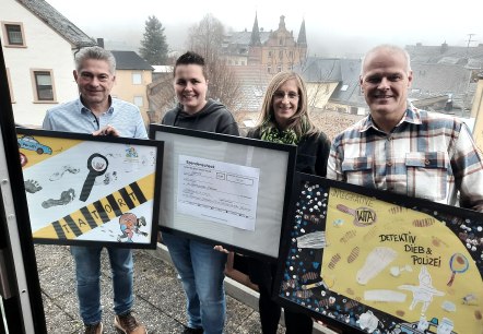 v.l.n.r.: Frank Reuter, Geschäftsführer Touristik GmbH Gerolsteiner Land, Jennifer Utecht, Leitung Integrative Kindertagesstätte Hillesheim, Steffi Götten, Leitung Kita Kunterbunt Hillesheim, Wolfgang Heck, 1. Vorsitzender Urlaubsregion Hillesheim, © Touristik GmbH Gerolsteiner Land 4 Personen stehen auf einem Balkon oberhalb einer Stadt. Sie halten 3 eingerahmte Bilder in den Händen. 2 der Bilder sind von Kindern gebastelte Collagen und das Bild in der Mitte zeigt einen Spendenscheck.