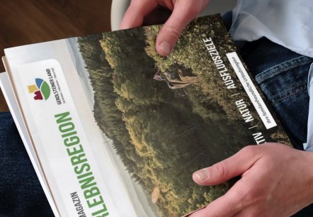 De brochure “Gästemagazin Erlebenisregion Gerolsteiner Land” (Gastenmagazine Erlebenisregion Gerolsteiner Land) wordt omhooggehouden., © Touristik GmbH Gerolsteiner Land De brochure “Gästemagazin Erlebenisregion Gerolsteiner Land” (Gastenmagazine Erlebenisregion Gerolsteiner Land) wordt omhooggehouden.