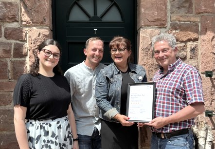 Succesvolle classificatie van de vakantiewoningen op Hof Grindelborn, Mürlenbach.
, © Hof Grindelborn Vier gelukkige en lachende mensen staan voor een toegangsdeur en houden trots het certificaat voor de classificatie in hun handen.