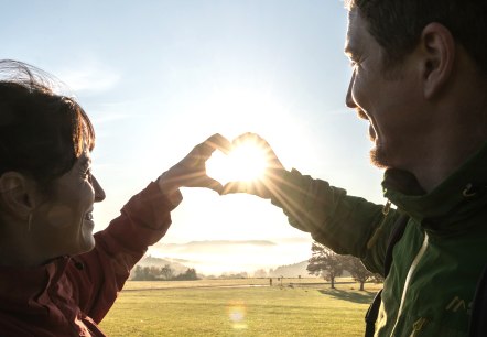 Two hikers on a vast meadow form a heart shape with their hands.
, © Eifel Tourismus GmbH, Dominik Ketz Two hikers on a vast meadow at sunrise form a heart shape with their hands.