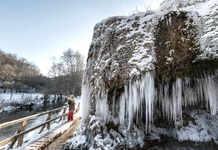 Frozen Nohner waterfall with icicles.
, © Eifel Tourismus GmbH, Dominik Ketz Frozen Nohner waterfall with icicles, a person on a footbridge, winter landscape with snow and bare trees.