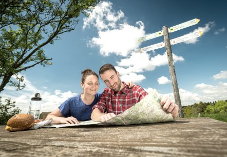 Two people take a break from their hike and look at a hiking map.
, © Eifel Tourismus GmbH, Dominik Ketz A man and a woman sit at a table in nature with food and drinks on the table. They study a hiking map.