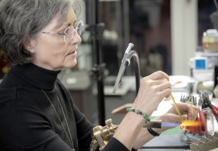 Beate Kloep bei der Arbeit.
, © Beate Kloep Eine Dame sitzt an einem Tisch und arbeitet konzentriert mit einem Brenner und Glas.