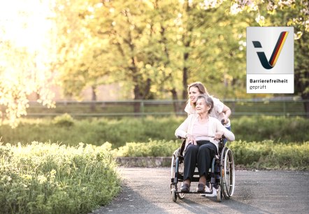 Uw barrièrevrije vakantie in het Gerolsteiner Land
, © Canva Een oudere dame in een rolstoel wordt door een jongere vrouw over een door weiden omgeven pad geduwd. De twee zijn in een goede stemming. Naast hen staat het logo “Toegankelijkheid getest”.