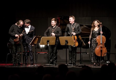 Christoph Soldan & die Schlesischen Kammersolisten, © Bildrechte Soldan, Fotograf Roman Huzior Fünf Musikanten auf einer Bühne mit Streichinstrumenten in der Hand stehen nebeneinander und lachen.