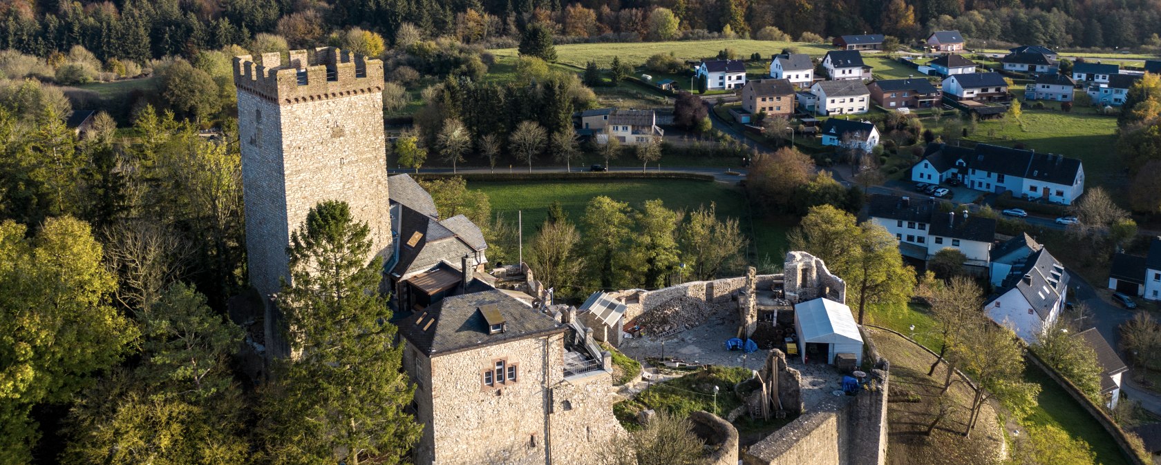 Burg Kerpen, © Eifel Tourismus GmbH, Dominik Ketz Eine nur noch in Teilen erhaltene Burg steht auf einer Anhöhe und thront über einem Dorf. Um das Dorf herum ist ein dichter Wald.