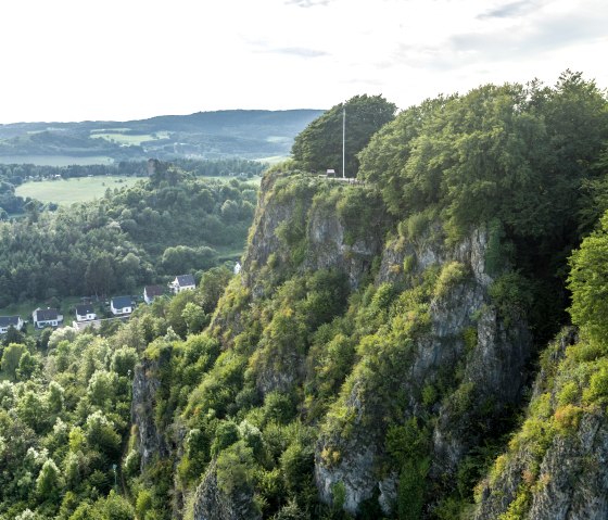 Luftaufnahme der Munterley Felsen bei Gerolstein. Bewaldete Klippen erheben sich über ein Tal mit Häusern. Im Hintergrund sind Hügel und Wälder zu sehen., © Eifel Tourismus GmbH, Dominik Ketz Luftaufnahme der Munterley Felsen bei Gerolstein. Bewaldete Klippen erheben sich über ein Tal mit Häusern. Im Hintergrund sind Hügel und Wälder zu sehen., © Eifel Tourismus GmbH, Dominik Ketz
