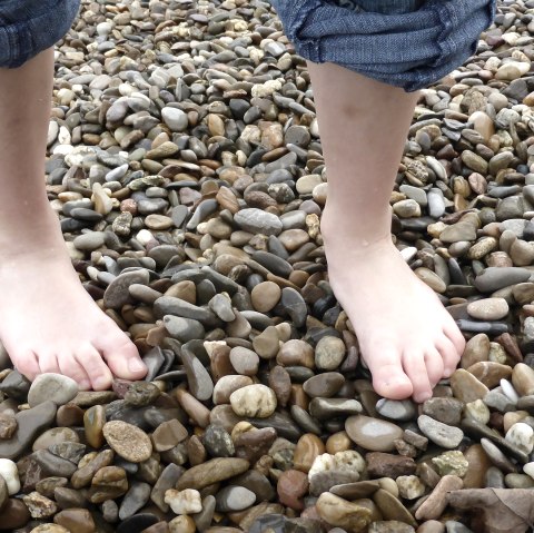 Two bare feet are standing on a pebble beach. The person is wearing rolled-up jeans., © pixabay Two bare feet are standing on a pebble beach. The person is wearing rolled-up jeans., © pixabay