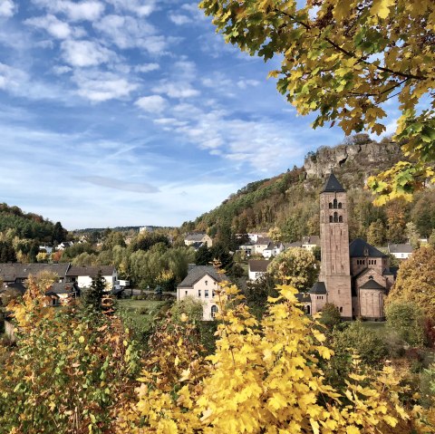 Erlöserkirche im Herbst Blick auf mehrere Wohnhäuser und eine große Kirche, die hervorstiecht. Rundherum Wiesen und Bäume in herbstlicher Atmosphäre. Oberhalb der Stadt ragen Felsen in die Höhe.
