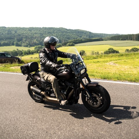 Motorcycle tour through the Eifel
, © Thomas Hendele A man wearing leather clothing and a helmet sits on a motorbike and rides along a road next to a wide meadow. A car is parked at the side of the road.