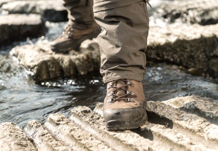 Ein Wanderstiefel steht auf einem Felsen über einem fließenden Bach. Der Stiefel ist braun und die Hose ist beige., © Eifel Tourismus GmbH, Dominik Ketz Ein Wanderstiefel steht auf einem Felsen über einem fließenden Bach. Der Stiefel ist braun und die Hose ist beige., © Eifel Tourismus GmbH, Dominik Ketz