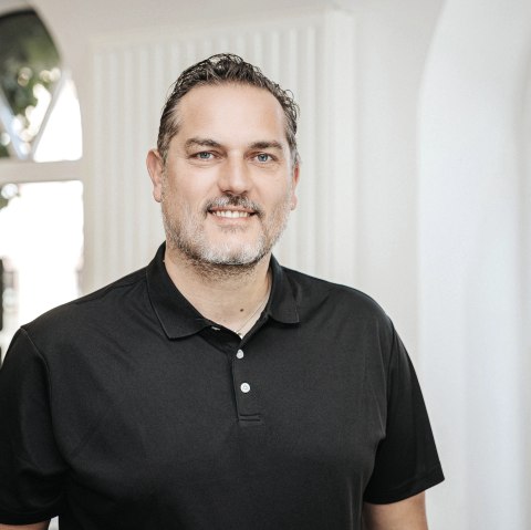 Kevin Hopp, medewerker van Touristik GmbH Gerolsteiner Land, stelt zich voor.
, © Laura Kirwel Een man staat achter een toonbank en glimlacht naar de camera. Achter hem staan enkele ramen en schappen met regionale producten.