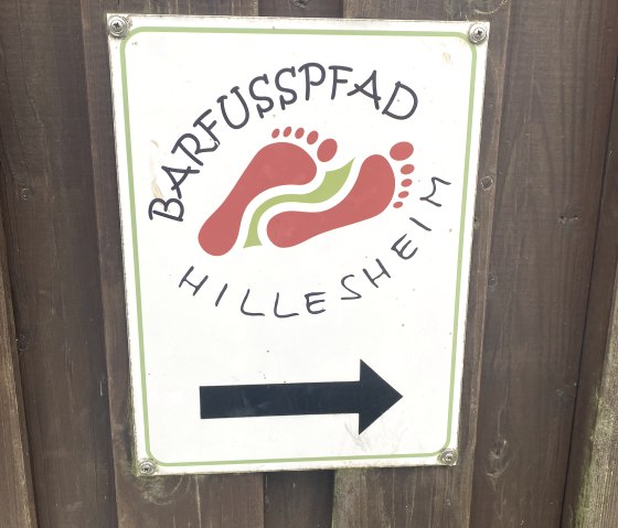 Sign with the inscription 'Barfußpfad Hillesheim' and an arrow pointing to the right on a wooden wall., © Touristik GmbH Gerolsteiner Land Sign with the inscription 'Barfußpfad Hillesheim' and an arrow pointing to the right on a wooden wall., © Touristik GmbH Gerolsteiner Land