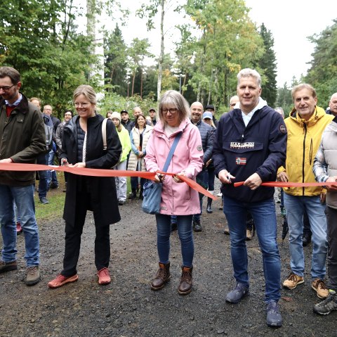 Landtagsabgeordneter Jens Jenssen, Landrätin Julia Gieseking, Verbandsgemeindebürgermeister Hans Peter Böffgen, Geschäftsführer Frank Reuter und Stadtbürgermeisterin Steffi Lorisch durchschneiden gemeinsam das rote Band und geben damit die Waldkugelbahn offiziell frei., © Thomas Langens Fünf Personen mit Scheren in den Händen durchschneiden gleichzeitig ein rotes Band. Hinter ihnen zahlreiche Zuschauer und Kinder.