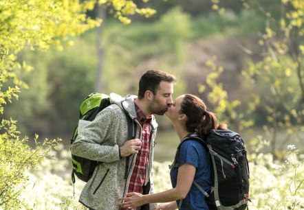Zwei Wanderer innmitten einer blühenden Wiese geben sich einen Kuss.
, © Eifel Tourismus GmbH, Dominik Ketz Blühende grüne Wiesen und Sträucher und mitten darin zwei Wanderer auf dem Weg, die sich einen Kuss geben.