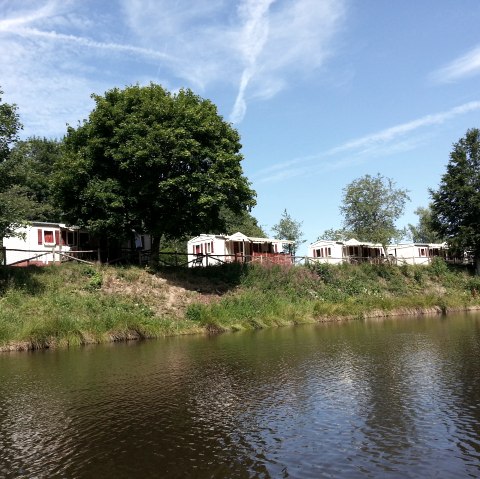 The reservoir in Landalpark Wirfttal with some holiday homes on the shore., © Touristik GmbH Gerolsteiner Land The reservoir in Landalpark Wirfttal with some small white identical holiday homes on the shore on a meadow. In between some trees and a blue sky.