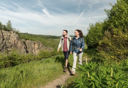 Wandelaars in de Steffelnvulkaan tuin voor de Steffelnkopf vulkaan., © Eifel Tourismus GmbH, Dominik Ketz Twee wandelaars midden in de natuur op een wandelpad. Op de achtergrond is een grote rotswand te zien. Dit is de Steffelnkopf vulkaan.