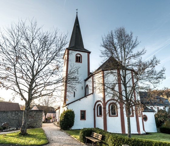 The monastery church in Niederehe with its high tower stands behind two bare trees next to the cemetery., © Eifel Tourismus GmbH, Dominik Ketz The monastery church in Niederehe with its high tower stands behind two bare trees next to the cemetery., © Eifel Tourismus GmbH, Dominik Ketz