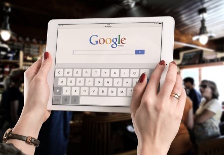 Google Suche, © pixabay Nahaufnahme zweier Hände, die ein Tablet halten, auf dem Google geöffnet ist.