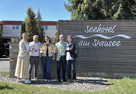 Herr Schinagl, Frau Funke und die Touristik GmbH Gerolsteiner Land freuen sich über das tolle Sterneergebnis., © Seehotel am Stausee Fünf Personen stehen vor der Fassade des Seehotels am Stausee in gerolstein und halten jeweils 4 Sterne und ein "S" für die Sterneklassifizierung hoch.