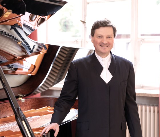 Christoph Soldan am Flügel
, © Soldan Ein Mann steht neben einem Flügel und schaut lachend in die Kamera