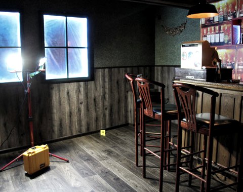 Escape Room Unter Verdacht im EifelKrimihotel Hillesheim.
, © EIFELkrimihotel Spärlich beleuchteter Raum mit Theke und Thekenstühlen, zugeklebter Fensterscheibe und Couchbereích.