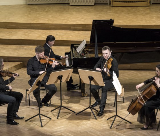 Christoph Soldan und die Schlesischen Kammersolisten beim musizieren
, © Soldan 4 Personen an Streichinstrumenten und ein Mann am Flügel musiziere gemeinsam auf einer Bühne.