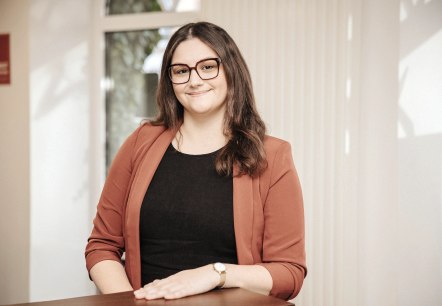 Elvira Weimer, medewerkster van Touristik GmbH Gerolsteiner Land, stelt zich voor.
, © Laura Kirwel Een vrouw staat achter een balie in een lichte kantoorruimte en glimlacht naar de camera. Achter haar zijn enkele ramen te zien.