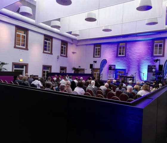 Das Publikum bei den Hillesheimer Krimitagen 2023, © Touristik GmbH Gerolsteiner Land, Nadja Blum Publikum in einem schwach beleuchteten Veranstaltungsraum mit Blick zur Bühne