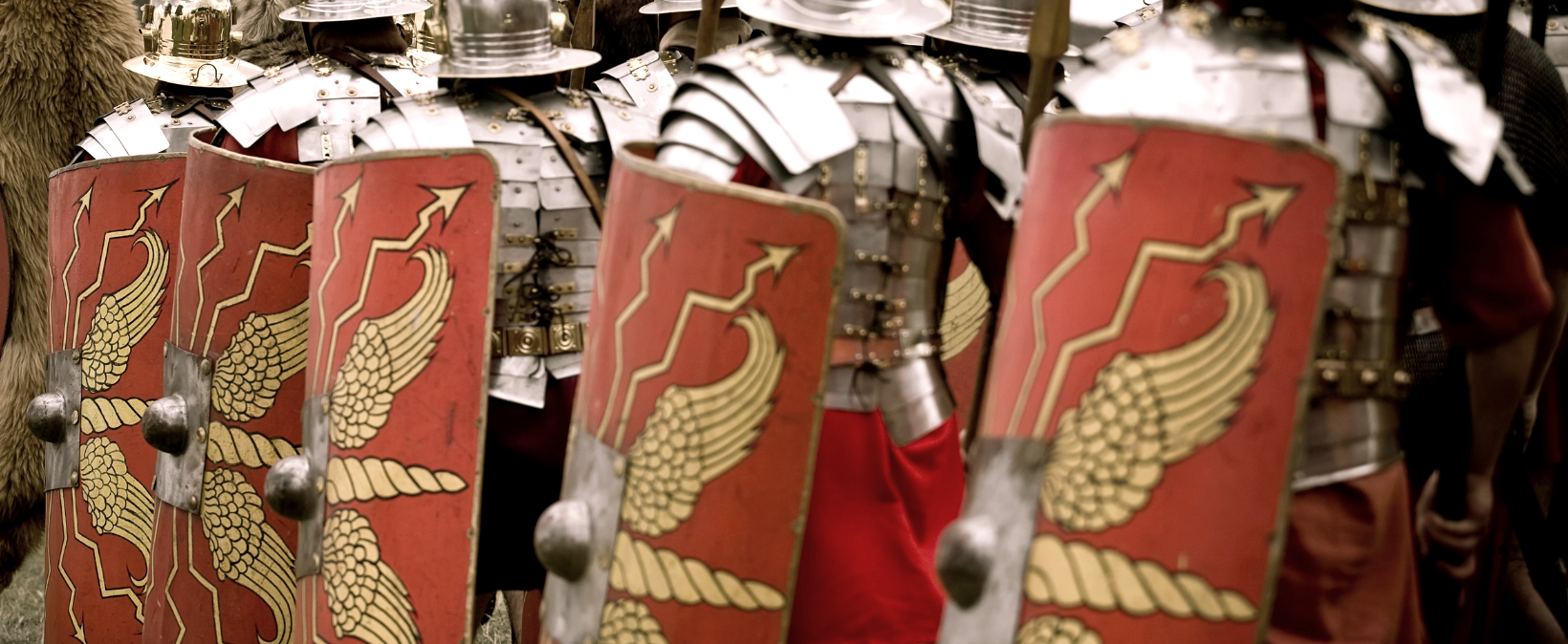 Musterbild Römertrupp, © canva Eine Truppe Männer in Rüstungen gekleidet und mit Schildern und Speren ausgestattet