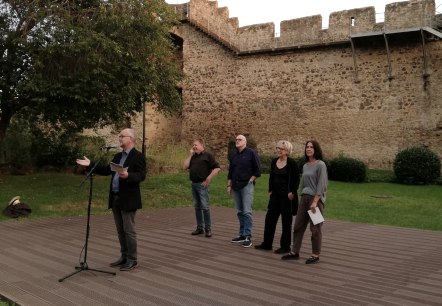 Hillesheimer Krimitage Evenement voor de stadsmuur van Hillesheim, © Touristik GmbH Gerolsteiner Land, Nadja Blum Vijf personen op een plat openluchtpodium voor de stadsmuur van Hillesheim