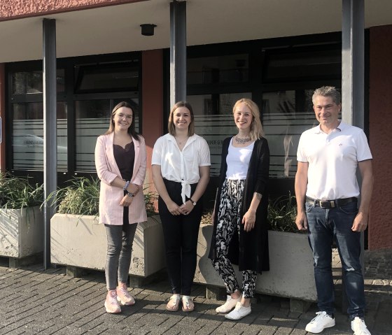 Begrüßung der neuen Mitarbeiterinnen der Touristik GmbH Gerolsteiner Land durch Geschäftsführer Frank Reuter.
, © Touristik GmbH Gerolsteiner Land Drei Frauen und ein Mann stehen nebeneinander vor einem Gebäude und lächeln in die Kamera.