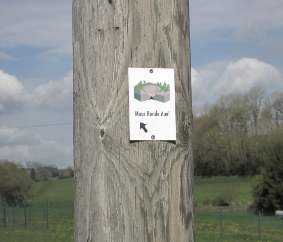 A wooden post with a sign 'Maar Runde Auel' and an arrow. Green meadows and trees can be seen in the background., © Touristik GmbH Gerolsteiner Land, Ute Klinkhammer A wooden post with a sign 'Maar Runde Auel' and an arrow. Green meadows and trees can be seen in the background., © Touristik GmbH Gerolsteiner Land, Ute Klinkhammer