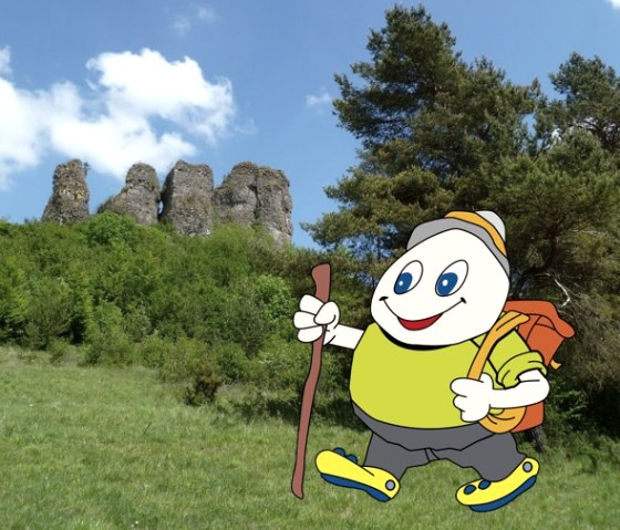 Family-friendly mascot Willi Basalt hikes through the Gerolstein region, © Touristik GmbH Gerolsteiner Land Cartoon character Willi Basalt with green shirt, grey trousers and yellow shoes and rucksack is hiking in a meadow. Above him is the ‘Auberg’ rock formation in Gerolstein.