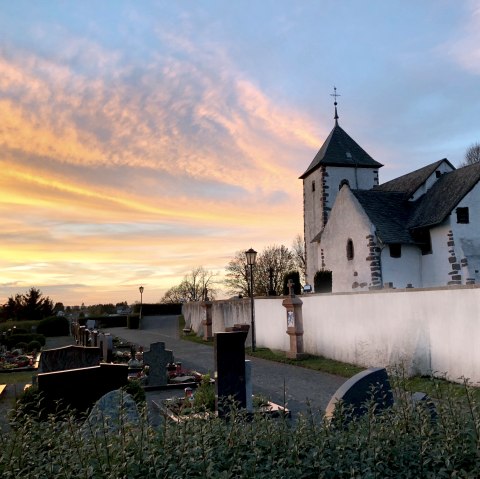 Eine Wehrkirche bei Sonnenuntergang, umgeben von einem Friedhof. Der Himmel ist in warmen Orange- und Blautönen gefärbt. Eine Wehrkirche bei Sonnenuntergang, umgeben von einem Friedhof. Der Himmel ist in warmen Orange- und Blautönen gefärbt.