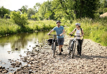 Two cyclists push their bikes over stones on the banks of the Kyll in Stadtkyll spa gardens.
, © Eifel Tourismus GmbH Gerolsteiner Land A man and a woman push their bikes over stones on the banks of the river in Stadtkyll spa gardens.