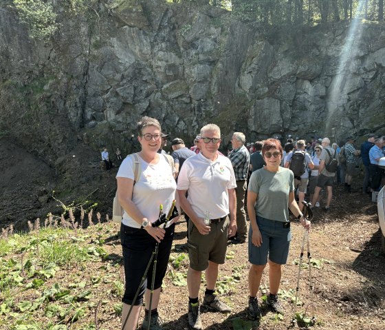 Frank Reuter und Team am Vulkantag 2025, © Touristik GmbH Gerolsteiner Land Zahlreiche Wanderer vor einer massiven Steinwand. Im Vordergrund 3 Wanderer nebeneinander.
