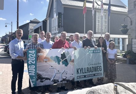 Press event for the Boundless Kyll Cycle Route Cycling Day
, © Gemeinde Hellenthal Thirteen people stand close together, holding up a banner for the Boundless Kyll Cycle Route Cycling Day on 11 August 2024.