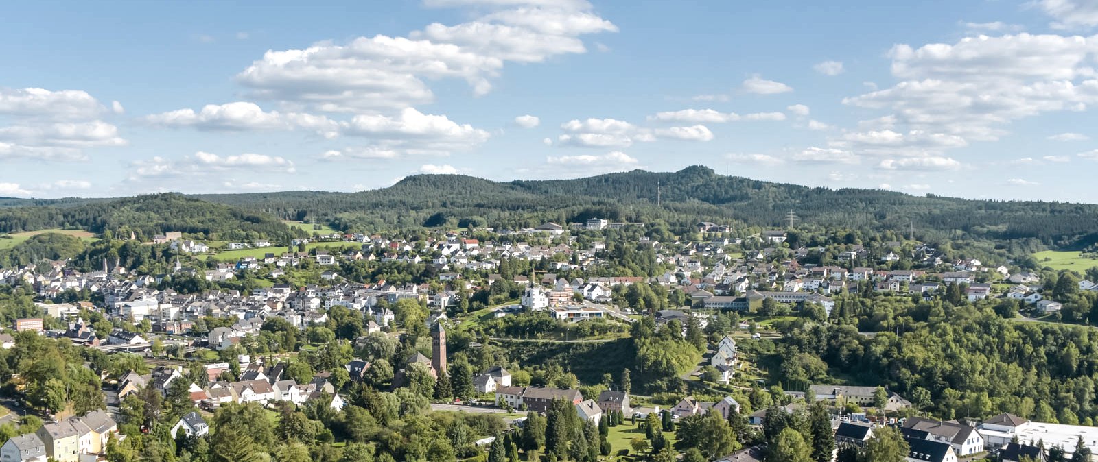 Blick über die Stadt Gerolstein mit zahlreichen Gebäuden, grünen Bäumen und Bergen im Hintergrund.
, © Thomas Hendele (alle Rechte vorbehalten) Blick über die Stadt Gerolstein mit zahlreichen Gebäuden, umgeben von grünen Bäumen und Bergen im Hintergrund.