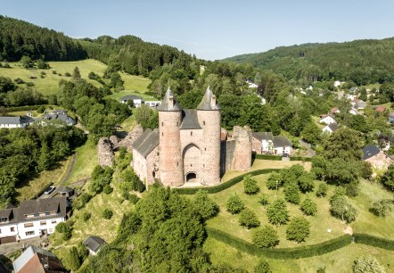 Aerial view of Bertrada Castle in Mürlenbach, surrounded by green countryside and houses. The castle has two striking towers., © Eifel Tourismus GmbH, Dominik Ketz Aerial view of Bertrada Castle in Mürlenbach, surrounded by green countryside and houses. The castle has two striking towers., © Eifel Tourismus GmbH, Dominik Ketz