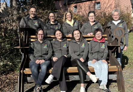 Group photo of the Gerolsteiner Land Tourism Ltd team wearing their new matching team jackets.
, © Touristik GmbH Gerolsteiner Land A group of nine people, some of whom are sitting on a bench, smile at the camera. Everyone is wearing the same jacket with the company logo embroidered on it.