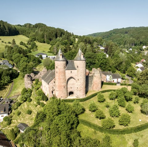 Luchtfoto van Kasteel Bertrada in Mürlenbach, omgeven door groen landschap en huizen. Het kasteel heeft twee opvallende torens., © Eifel Tourismus GmbH, Dominik Ketz Luchtfoto van Kasteel Bertrada in Mürlenbach, omgeven door groen landschap en huizen. Het kasteel heeft twee opvallende torens., © Eifel Tourismus GmbH, Dominik Ketz