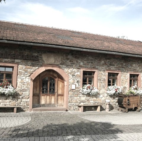 Standesamtgebäude auf dem Hof der historischen Wassermühle Birgel.
, © Spohr Ein eingeschossiges längliches Gebäude aus Bruchsteinen und mit einem rotem Ziegeldach. Vor den Fenstern sind Blumenkästen. Der Hof vor dem Gebäude ist gepflastert.