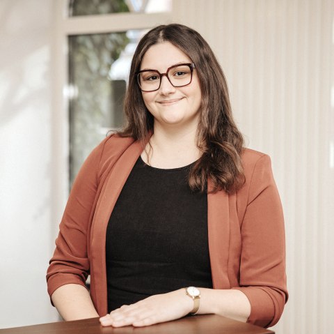 Elvira Weimer, Mitarbeiterin der Touristik GmbH Gerolsteiner Land, stellt sich vor.
, © Laura Kirwel Eine Frau steht hinter einem Tresen in einem hellen Büroraum und lächelt in die Kamera. Hinter ihr einige Fenster.